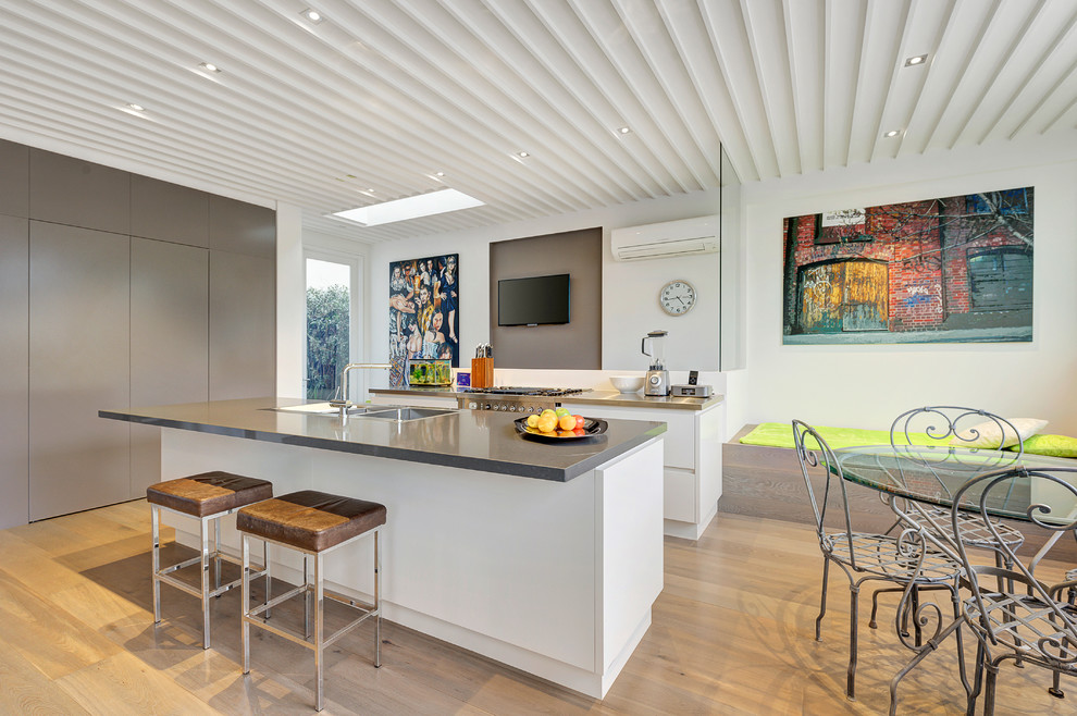 メルボルンにある広いコンテンポラリースタイルのおしゃれなキッチン (ダブルシンク、白いキャビネット、シルバーの調理設備、淡色無垢フローリング、フラットパネル扉のキャビネット) の写真