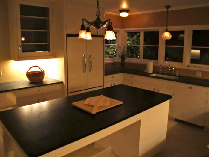 Immagine di un cucina con isola centrale con lavello sottopiano, ante bianche, top in saponaria, elettrodomestici da incasso e pavimento in pietra calcarea
