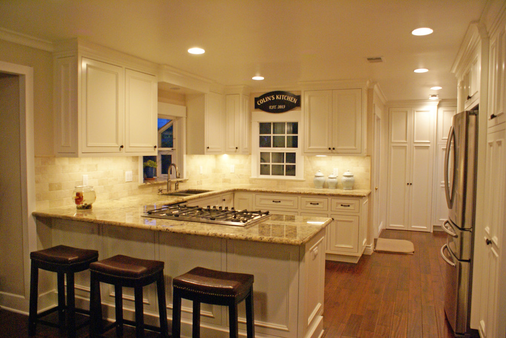 Example of a large arts and crafts u-shaped dark wood floor eat-in kitchen design in Los Angeles with an undermount sink, beaded inset cabinets, white cabinets, granite countertops, beige backsplash, stone slab backsplash, stainless steel appliances and a peninsula
