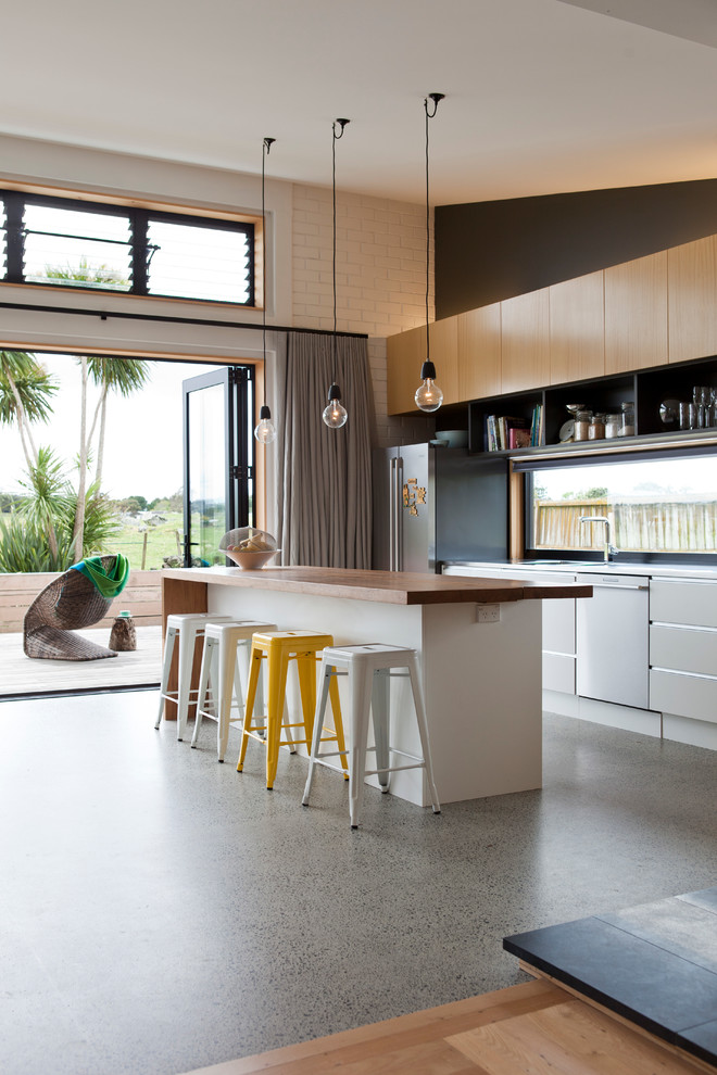 Imagen de cocina actual con armarios con paneles lisos, encimera de acero inoxidable, electrodomésticos de acero inoxidable y una isla