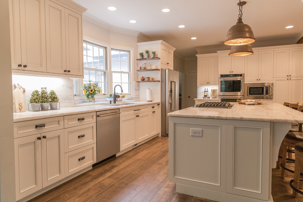 Inspiration for a country kitchen in Charlotte with a triple-bowl sink, recessed-panel cabinets, white cabinets, marble worktops, white splashback, marble splashback, stainless steel appliances, ceramic flooring, an island, brown floors and white worktops.