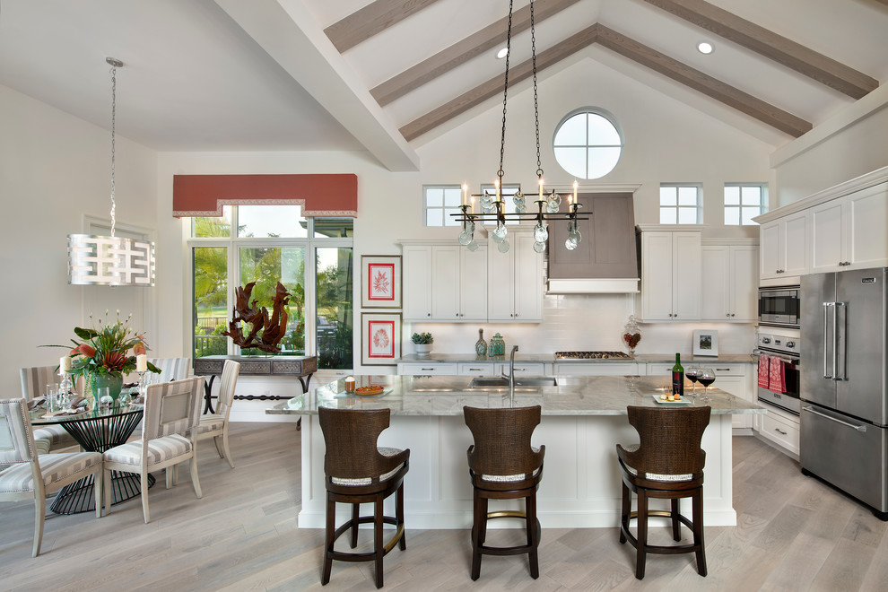 This is an example of a large world-inspired kitchen/diner in Tampa with white cabinets, granite worktops, white splashback, stainless steel appliances, light hardwood flooring, an island and shaker cabinets.