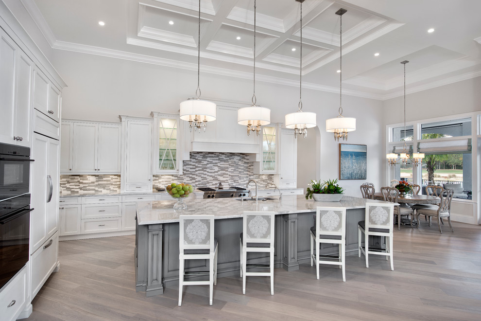Inspiration for a large timeless l-shaped light wood floor open concept kitchen remodel in Tampa with an island, a drop-in sink, white cabinets, gray backsplash, mosaic tile backsplash and paneled appliances