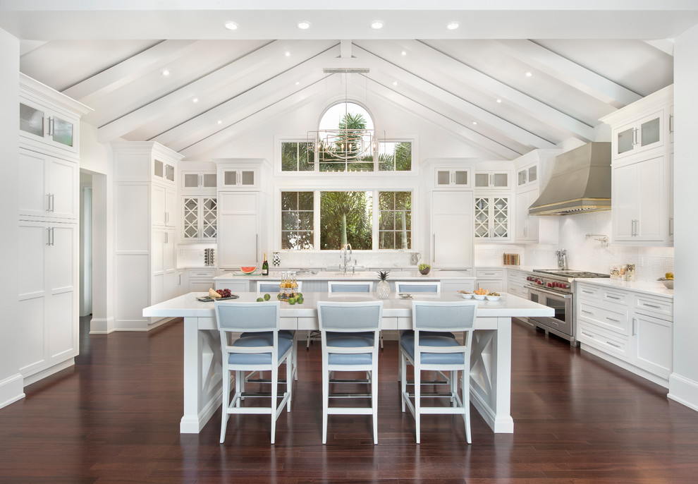 Große Küche mit weißen Schränken, zwei Kücheninseln, Glasfronten, Küchenrückwand in Weiß, Küchengeräten aus Edelstahl und braunem Holzboden in Miami