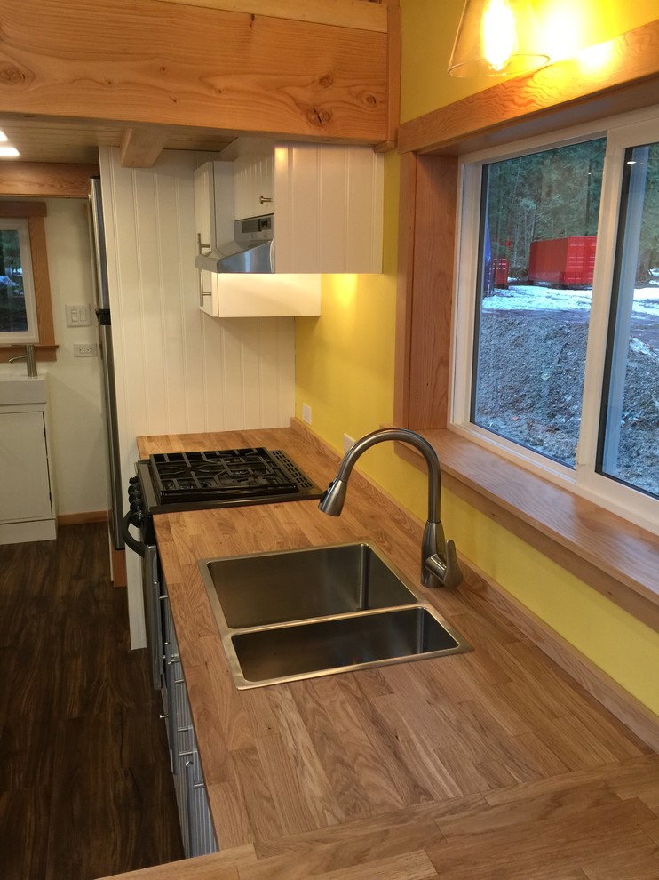 バンクーバーにある高級な小さなラスティックスタイルのおしゃれなキッチン (ダブルシンク、フラットパネル扉のキャビネット、白いキャビネット、木材カウンター、黄色いキッチンパネル、シルバーの調理設備、クッションフロア) の写真