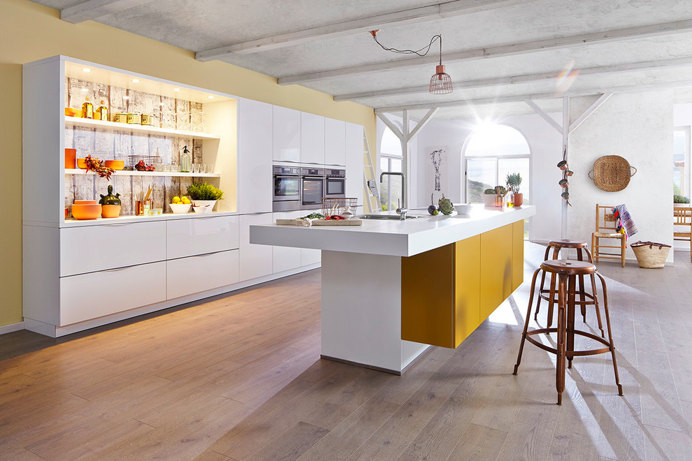 На фото: прямая кухня-гостиная среднего размера в современном стиле с белыми фасадами, островом, накладной мойкой, плоскими фасадами и техникой из нержавеющей стали с