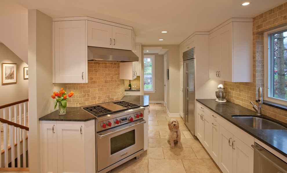 Exemple d'une cuisine chic avec un évier encastré, un placard à porte shaker, des portes de placard blanches, une crédence beige et un électroménager en acier inoxydable.