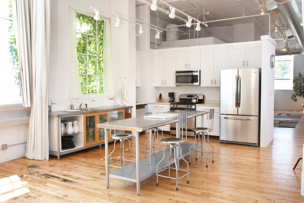 Exempel på ett industriellt l-kök, med skåp i shakerstil, vita skåp, rostfria vitvaror, mellanmörkt trägolv och en köksö