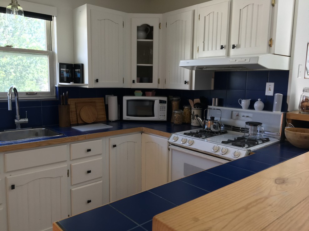 Inredning av ett klassiskt litet blå blått u-kök, med luckor med profilerade fronter, vita skåp, kaklad bänkskiva, blått stänkskydd, stänkskydd i keramik, laminatgolv och grått golv