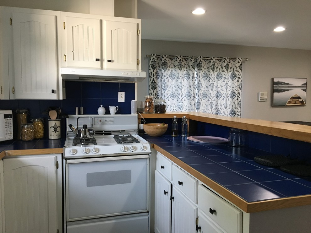 他の地域にある小さなトラディショナルスタイルのおしゃれなコの字型キッチン (インセット扉のキャビネット、白いキャビネット、タイルカウンター、青いキッチンパネル、セラミックタイルのキッチンパネル、ラミネートの床、グレーの床、青いキッチンカウンター) の写真