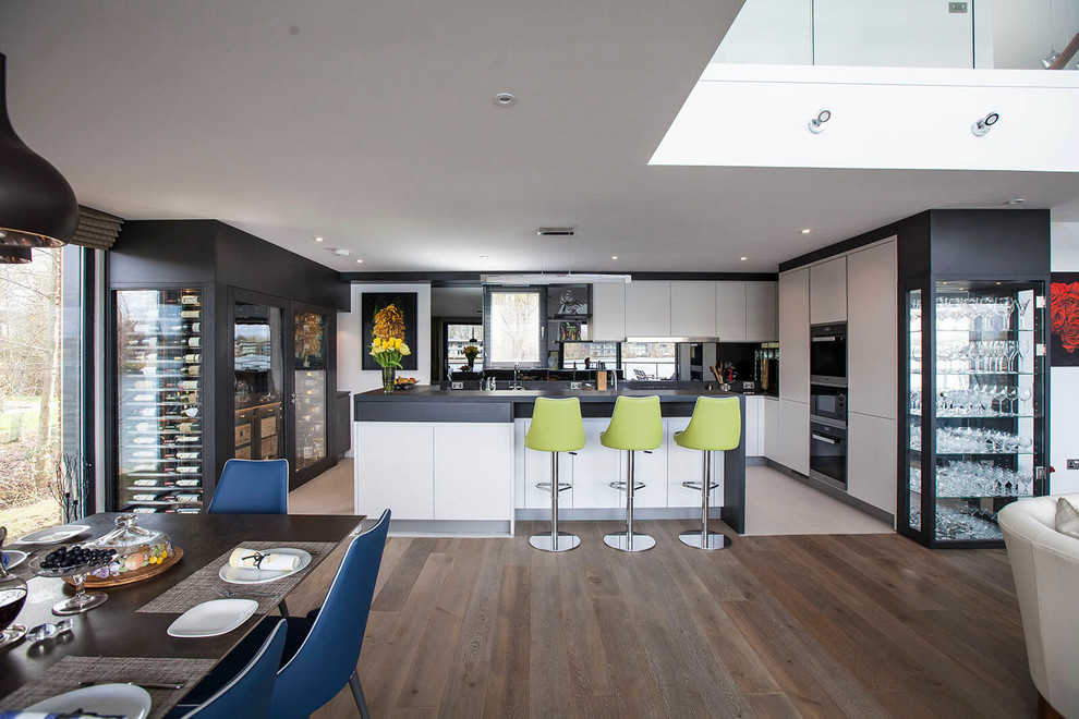 Offene, Geräumige Moderne Küche in U-Form mit flächenbündigen Schrankfronten, Kücheninsel, schwarzer Arbeitsplatte, schwarzen Elektrogeräten und weißem Boden in Essex
