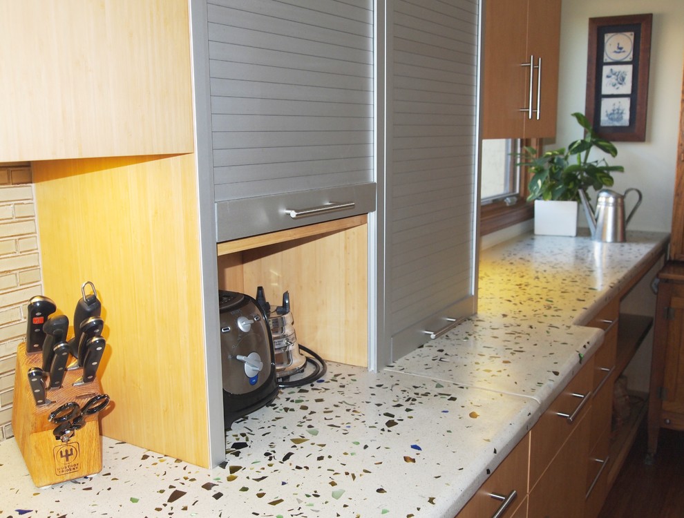 Cette photo montre une grande cuisine américaine linéaire moderne en bois clair avec un placard à porte plane, un plan de travail en verre recyclé, une crédence en carreau de verre, îlot, une crédence beige et un électroménager en acier inoxydable.