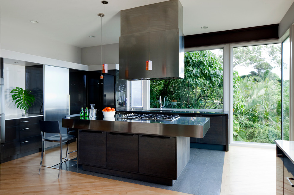 Modelo de cocina actual con encimera de acero inoxidable, armarios con paneles lisos, puertas de armario negras y electrodomésticos de acero inoxidable
