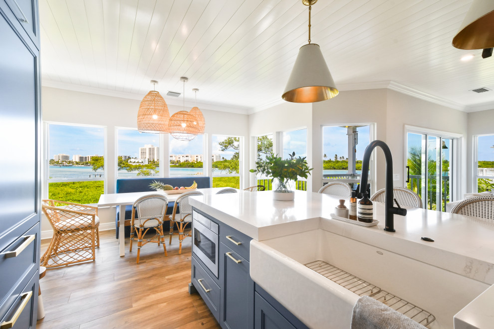 Mid-sized beach style l-shaped porcelain tile, brown floor and shiplap ceiling open concept kitchen photo in Other with a farmhouse sink, shaker cabinets, blue cabinets, quartz countertops, white backsplash, porcelain backsplash, black appliances, an island and white countertops