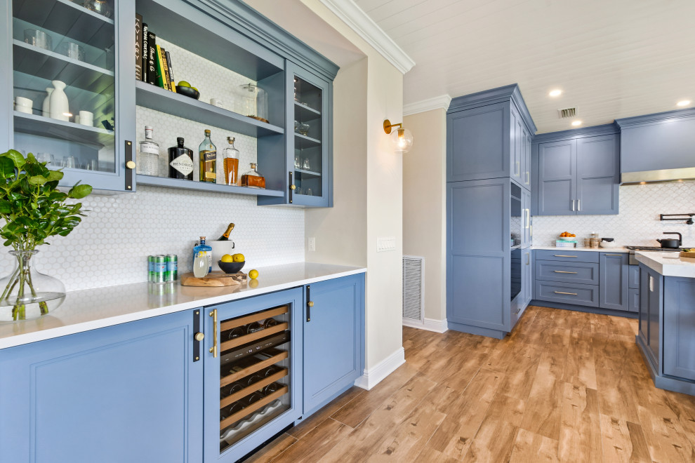 Example of a mid-sized beach style l-shaped porcelain tile, brown floor and shiplap ceiling open concept kitchen design in Other with a farmhouse sink, shaker cabinets, blue cabinets, quartz countertops, white backsplash, porcelain backsplash, black appliances, an island and white countertops