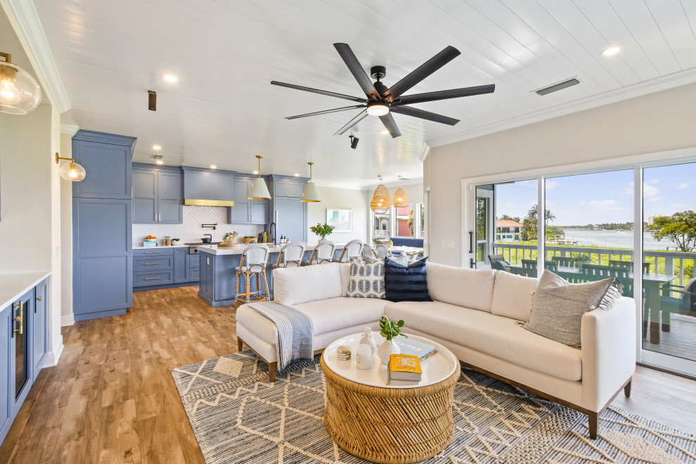 Mid-sized beach style l-shaped porcelain tile, brown floor and shiplap ceiling open concept kitchen photo in Other with a farmhouse sink, shaker cabinets, blue cabinets, quartz countertops, white backsplash, porcelain backsplash, black appliances, an island and white countertops