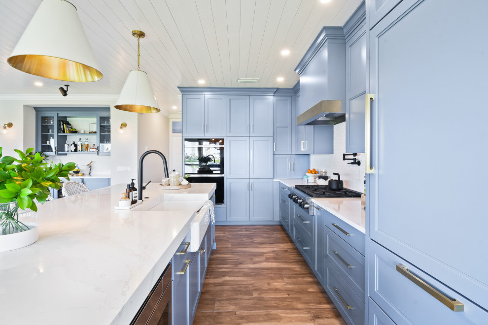 Mid-sized beach style l-shaped porcelain tile, brown floor and shiplap ceiling open concept kitchen photo in Other with a farmhouse sink, shaker cabinets, blue cabinets, quartz countertops, white backsplash, porcelain backsplash, black appliances, an island and white countertops