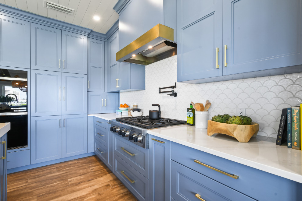 Mid-sized beach style l-shaped porcelain tile, brown floor and shiplap ceiling open concept kitchen photo in Other with a farmhouse sink, shaker cabinets, blue cabinets, quartz countertops, white backsplash, porcelain backsplash, black appliances, an island and white countertops