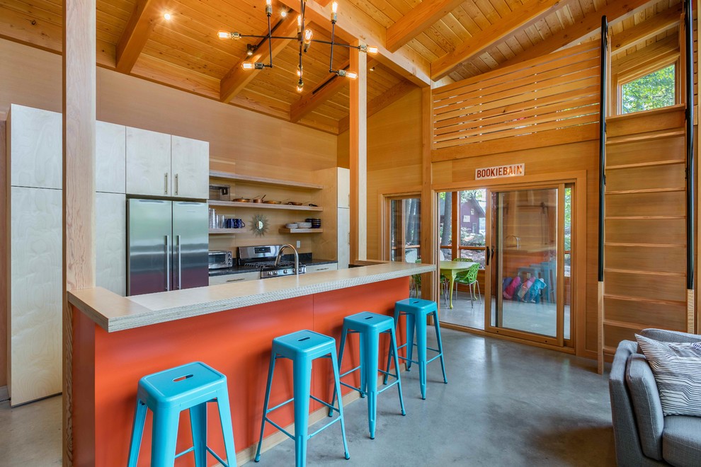 Example of a beach style concrete floor and gray floor open concept kitchen design with flat-panel cabinets, light wood cabinets, wood backsplash, stainless steel appliances and an island