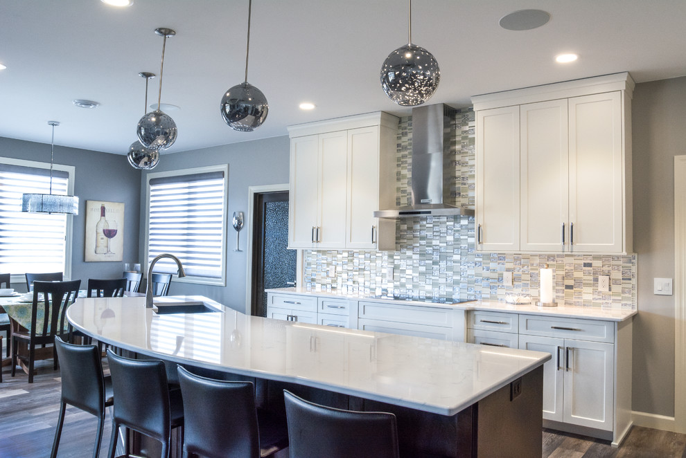 Example of a mid-sized trendy l-shaped medium tone wood floor and brown floor open concept kitchen design in Other with a double-bowl sink, white cabinets, quartz countertops, gray backsplash, stainless steel appliances, an island, shaker cabinets and matchstick tile backsplash