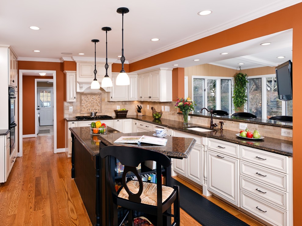 Example of a classic u-shaped light wood floor eat-in kitchen design in DC Metro with a drop-in sink, beaded inset cabinets, distressed cabinets, granite countertops, beige backsplash, ceramic backsplash, black appliances and an island