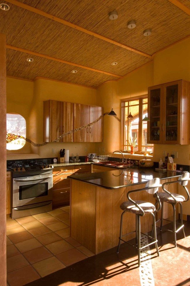 Eklektisk inredning av ett litet kök, med en nedsänkt diskho, släta luckor, skåp i mellenmörkt trä, bänkskiva i kvarts, svart stänkskydd, rostfria vitvaror, klinkergolv i keramik, en halv köksö och orange golv