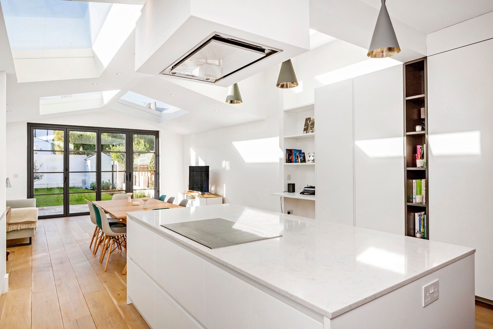 На фото: п-образная кухня-гостиная в современном стиле с плоскими фасадами, белыми фасадами, светлым паркетным полом, островом и коричневым полом