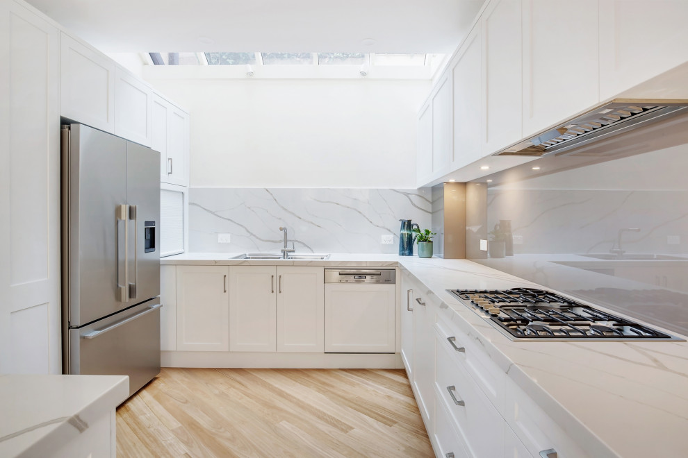 Klassisk inredning av ett mellanstort grå grått l-kök, med en nedsänkt diskho, skåp i shakerstil, vita skåp, grått stänkskydd, glaspanel som stänkskydd, rostfria vitvaror och beiget golv