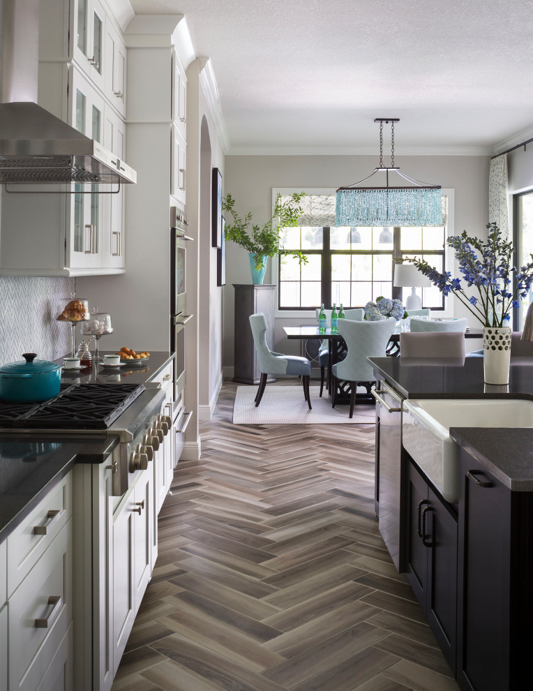 Example of a large classic l-shaped ceramic tile and gray floor open concept kitchen design in Tampa with a farmhouse sink, shaker cabinets, white cabinets, quartz countertops, white backsplash, marble backsplash, stainless steel appliances, an island and black countertops