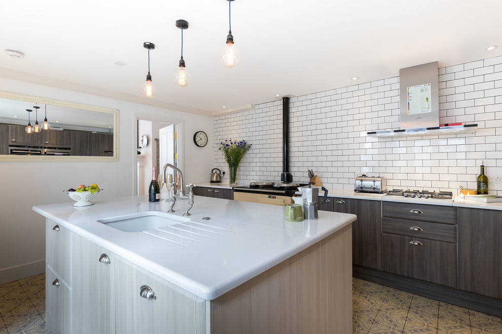 This is an example of a medium sized traditional l-shaped kitchen/diner in Sussex with a submerged sink, flat-panel cabinets, brown cabinets, composite countertops, white splashback, metro tiled splashback, coloured appliances, ceramic flooring, an island, multi-coloured floors and white worktops.