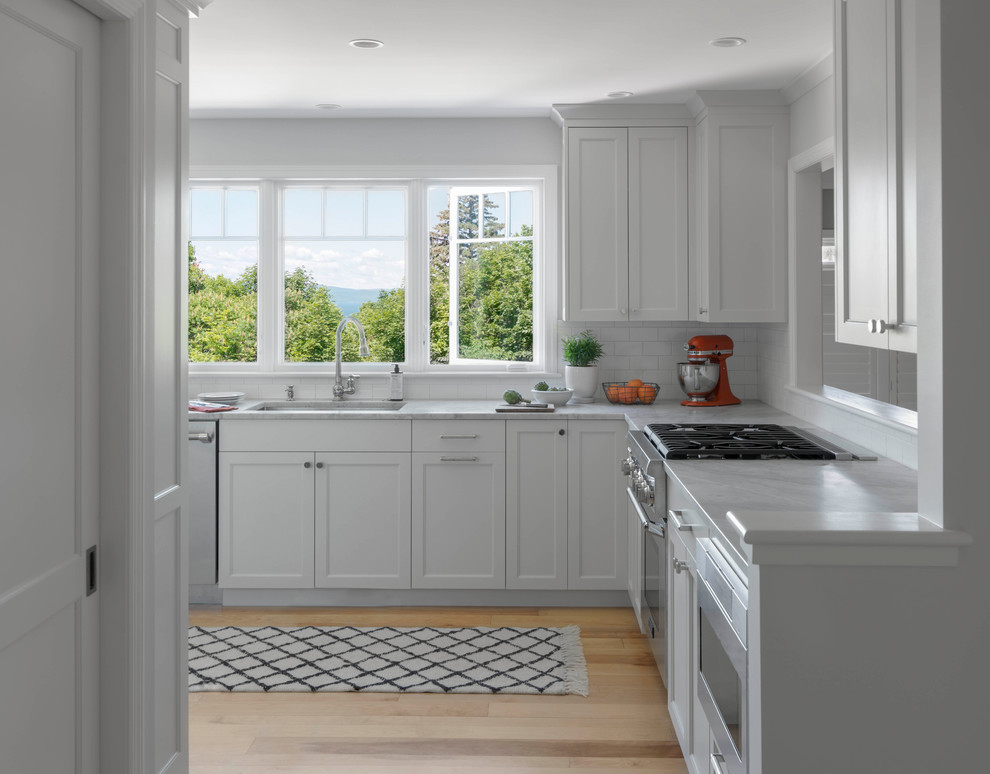 Idéer för mellanstora funkis grått kök, med en undermonterad diskho, luckor med infälld panel, vita skåp, granitbänkskiva, vitt stänkskydd, stänkskydd i keramik, rostfria vitvaror, ljust trägolv och en köksö