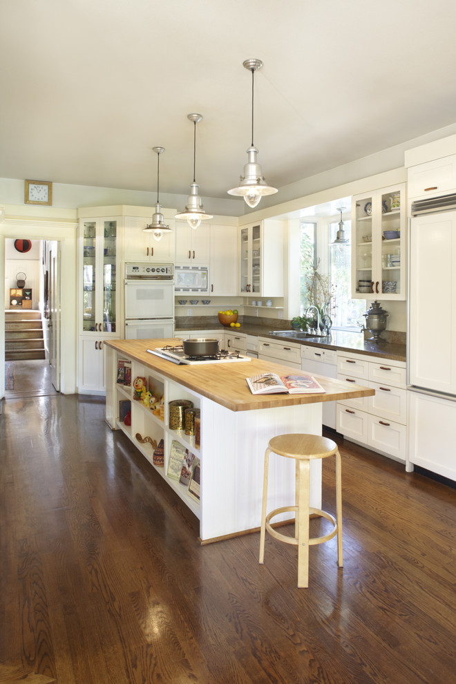Example of a mid-sized farmhouse l-shaped dark wood floor and brown floor eat-in kitchen design in San Francisco with wood countertops, an undermount sink, shaker cabinets, white cabinets, an island, paneled appliances and brown countertops