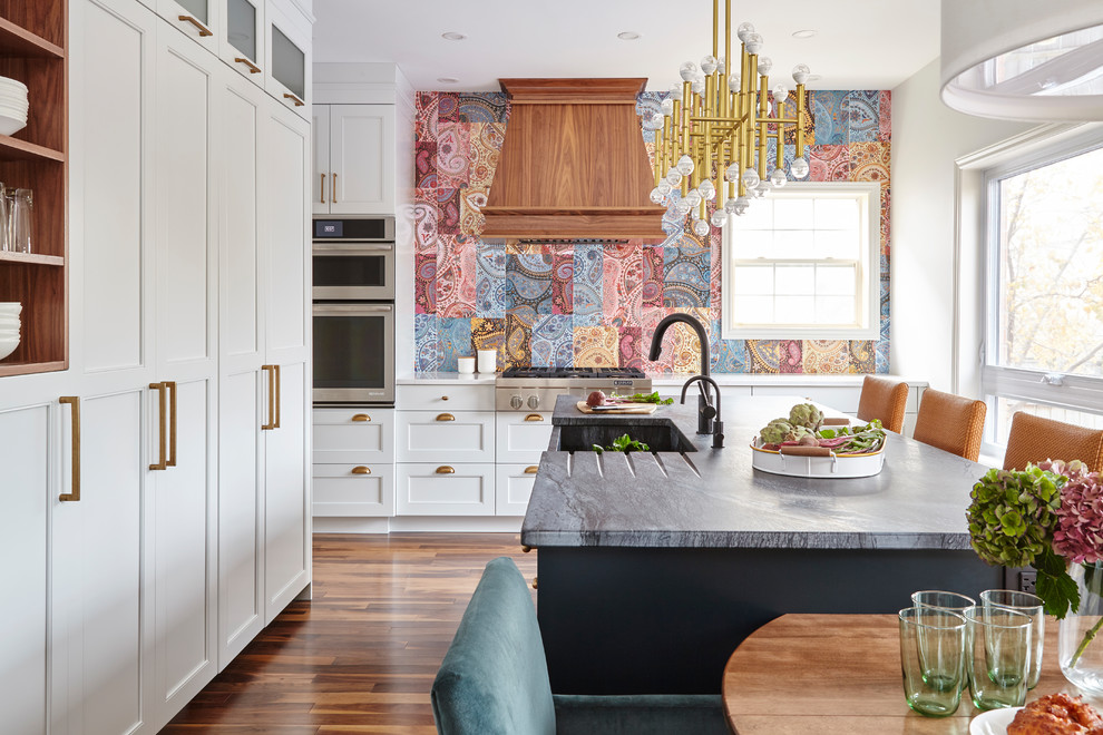 Klassische Wohnküche in L-Form mit Landhausspüle, Schrankfronten im Shaker-Stil, weißen Schränken, bunter Rückwand, braunem Holzboden, Kücheninsel und braunem Boden in Toronto