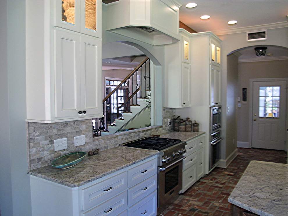 Eat-in kitchen - mid-sized transitional l-shaped brick floor eat-in kitchen idea in Other with recessed-panel cabinets, white cabinets, granite countertops, brown backsplash, stone tile backsplash, stainless steel appliances and an island