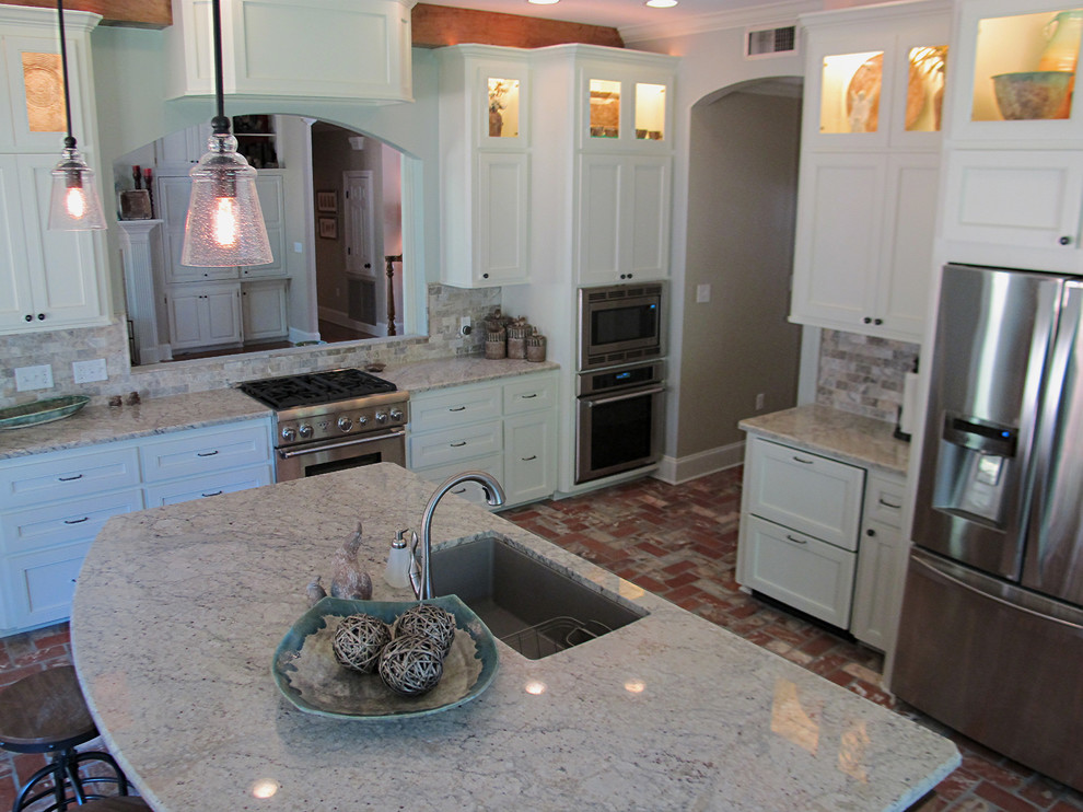 Foto på ett mellanstort vintage kök, med en undermonterad diskho, luckor med infälld panel, vita skåp, granitbänkskiva, brunt stänkskydd, stänkskydd i stenkakel, rostfria vitvaror, tegelgolv och en köksö