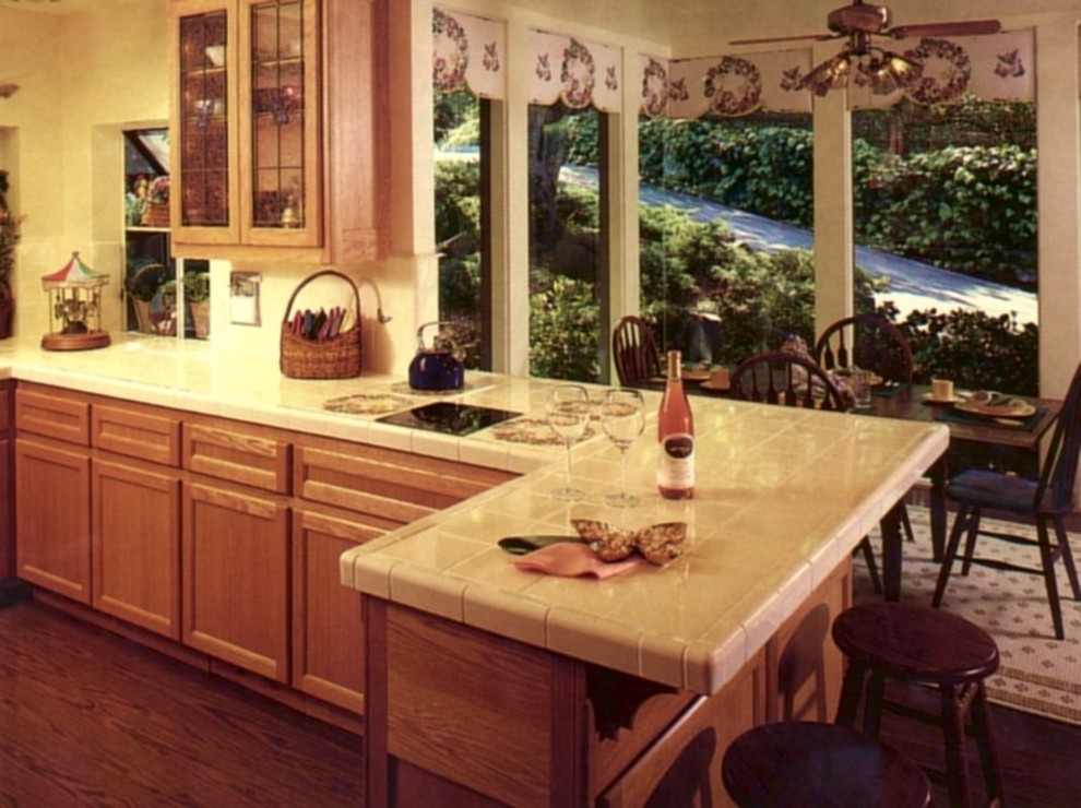 Example of a large eclectic u-shaped medium tone wood floor eat-in kitchen design in San Francisco with a triple-bowl sink, shaker cabinets, light wood cabinets, tile countertops, white backsplash, ceramic backsplash and stainless steel appliances