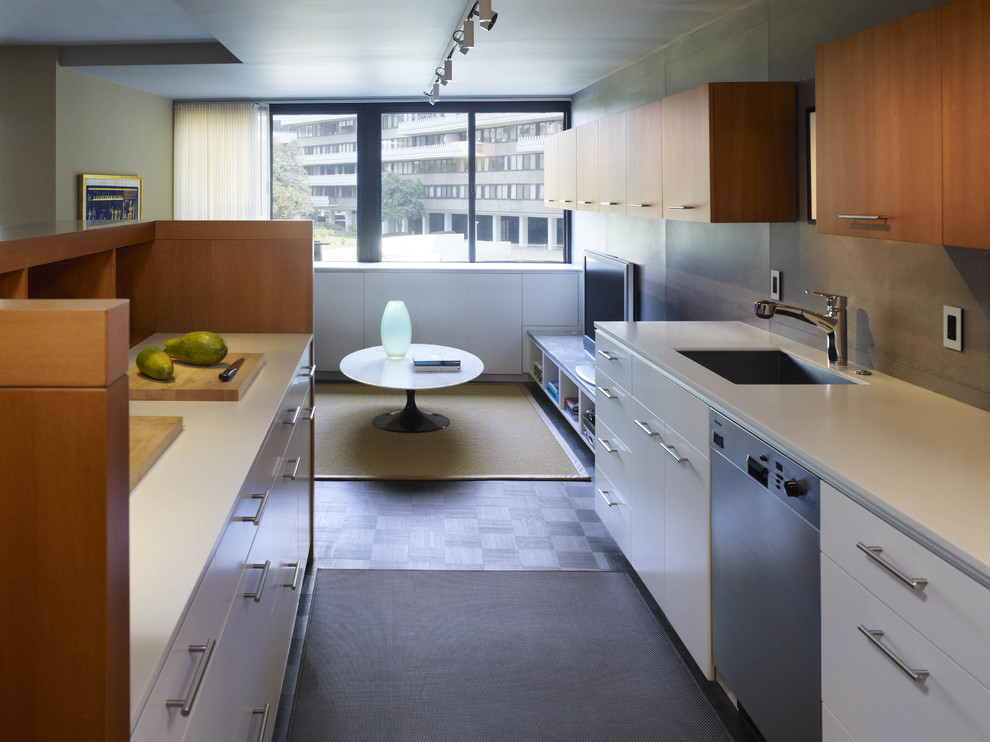 This is an example of a contemporary galley open plan kitchen in DC Metro with stainless steel appliances, a submerged sink, flat-panel cabinets, white cabinets, engineered stone countertops, grey splashback and cement tile splashback.