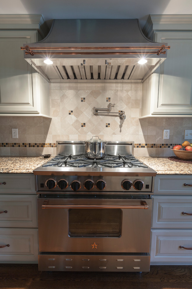 Inredning av ett klassiskt mellanstort kök, med en undermonterad diskho, luckor med upphöjd panel, vita skåp, bänkskiva i kvarts, vitt stänkskydd, stänkskydd i stenkakel, rostfria vitvaror, mellanmörkt trägolv och en halv köksö