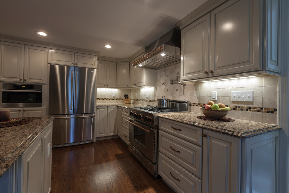 Example of a mid-sized classic l-shaped medium tone wood floor eat-in kitchen design in New York with an undermount sink, raised-panel cabinets, white cabinets, quartz countertops, white backsplash, stone tile backsplash, stainless steel appliances and a peninsula