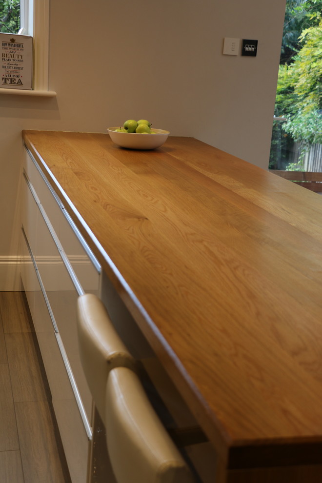 Foto di una cucina ad ambiente unico minimal di medie dimensioni con ante a filo, top in legno, parquet chiaro e penisola