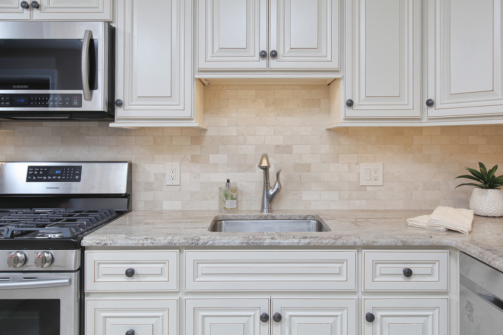Klassisk inredning av ett mellanstort kök, med en undermonterad diskho, luckor med upphöjd panel, vita skåp, granitbänkskiva, beige stänkskydd, rostfria vitvaror, en halv köksö, stänkskydd i stenkakel och klinkergolv i porslin