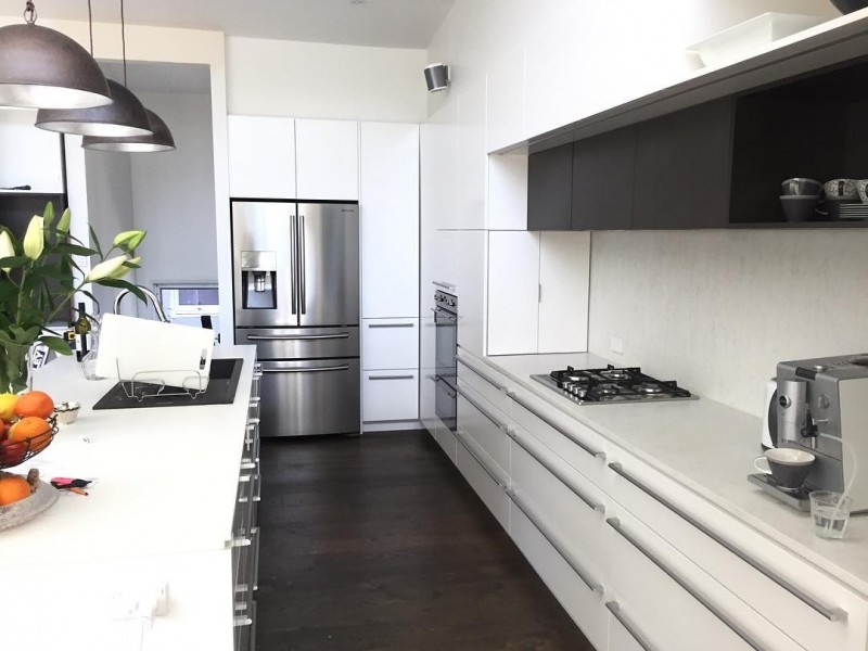 Foto på ett stort funkis vit kök, med en enkel diskho, vita skåp, marmorbänkskiva, vitt stänkskydd, stänkskydd i sten, rostfria vitvaror, mörkt trägolv och en köksö