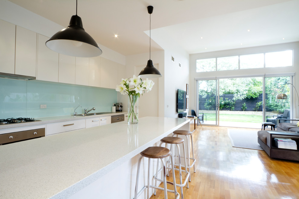 Inspiration for a contemporary single-wall open plan kitchen in Sussex with flat-panel cabinets, white cabinets, blue splashback, medium hardwood flooring, an island, brown floors and white worktops.