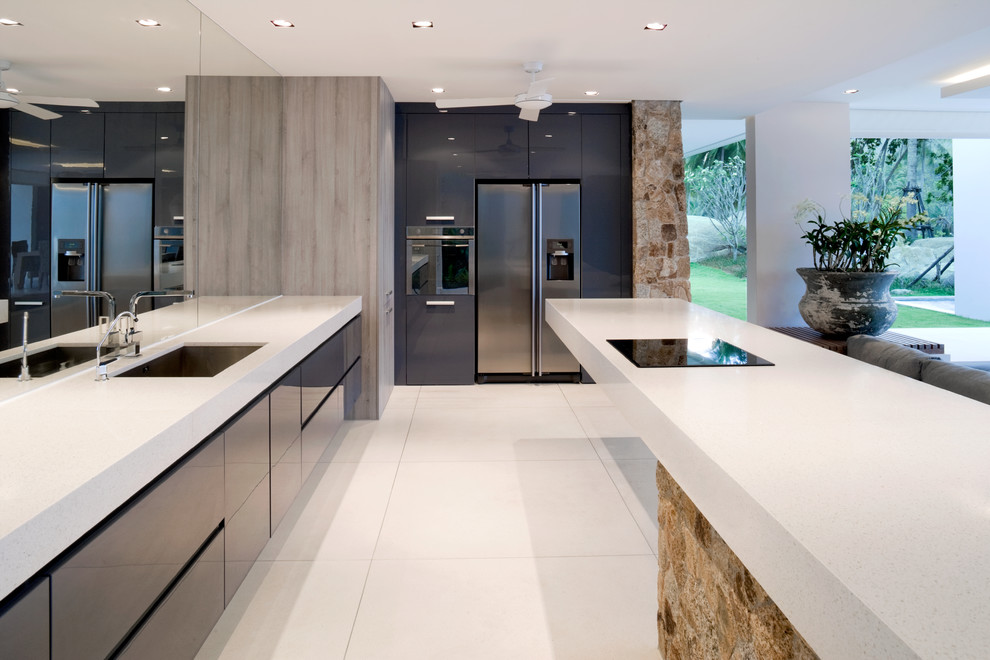 Trendy u-shaped white floor kitchen photo in Sussex with an undermount sink, flat-panel cabinets, black cabinets, stainless steel appliances and white countertops