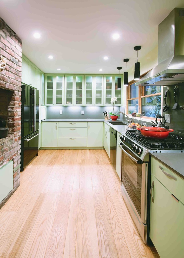 Modelo de cocinas en U contemporáneo cerrado con electrodomésticos negros, fregadero de doble seno, armarios tipo vitrina, puertas de armario verdes y salpicadero verde