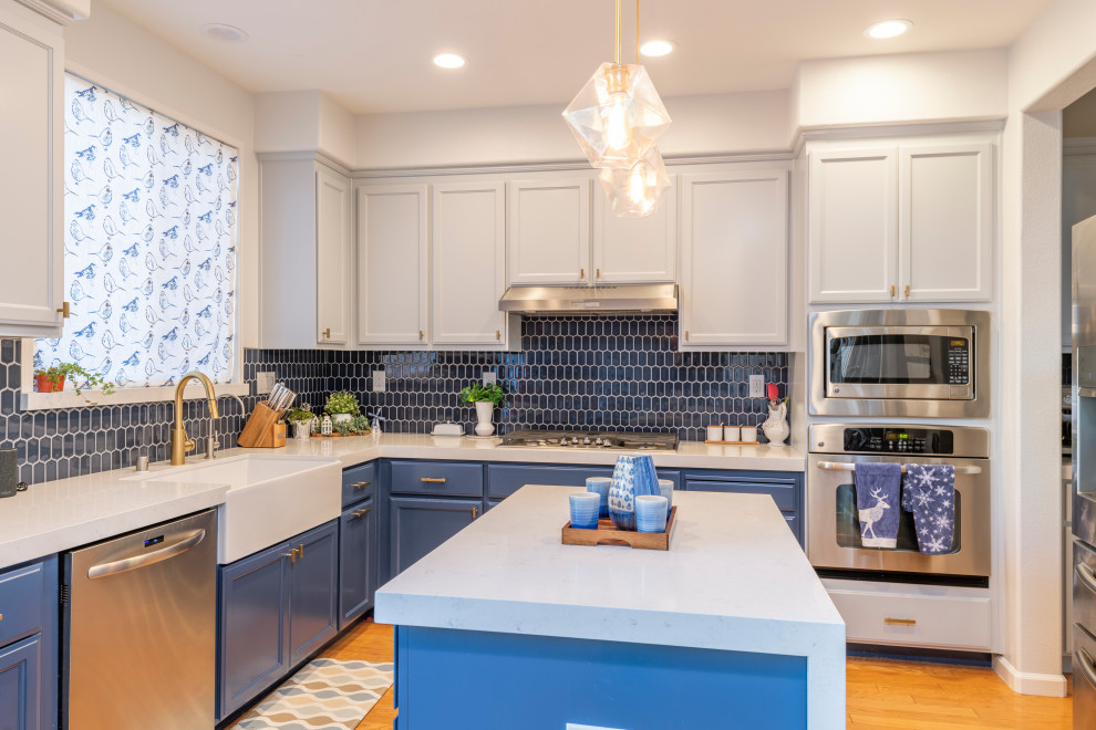 Classic l-shaped kitchen/diner in San Francisco with a belfast sink, grey cabinets, engineered stone countertops, blue splashback, mosaic tiled splashback, stainless steel appliances, an island and white worktops.