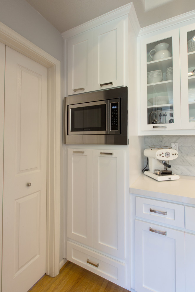 Bild på ett stort kök, med en undermonterad diskho, skåp i shakerstil, vita skåp, bänkskiva i kvarts, vitt stänkskydd och rostfria vitvaror
