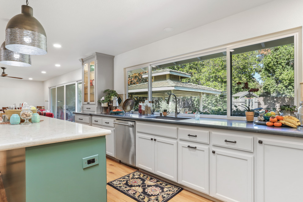 Large classic l-shaped kitchen/diner in Sacramento with a double-bowl sink, white cabinets, engineered stone countertops, beige splashback, travertine splashback, stainless steel appliances, laminate floors, an island, brown floors and grey worktops.