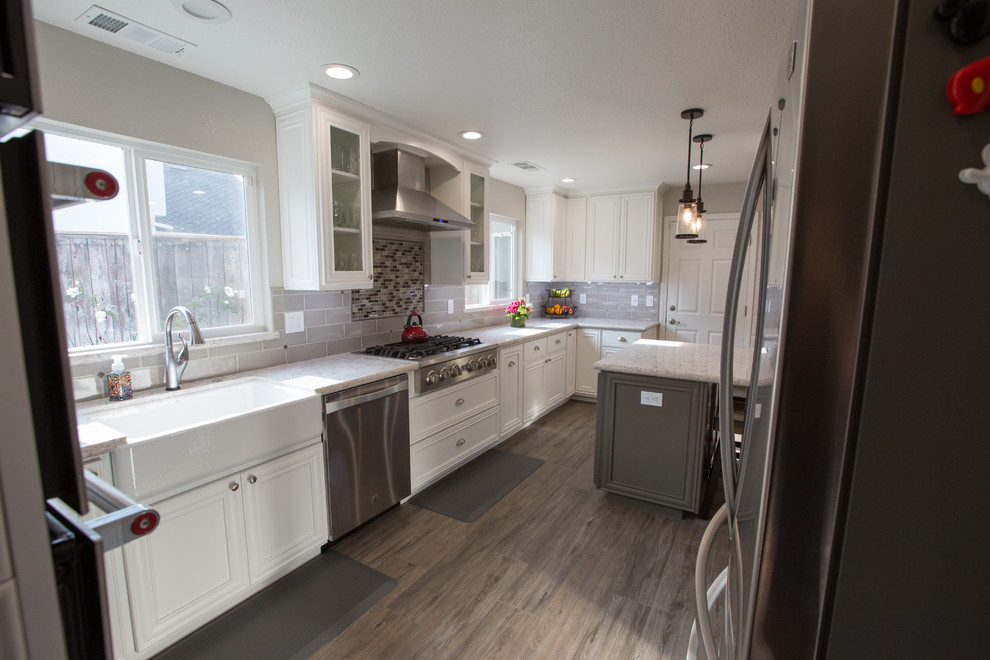 Modern kitchen in Sacramento with a belfast sink, white cabinets, engineered stone countertops, grey splashback, stainless steel appliances, ceramic flooring and an island.