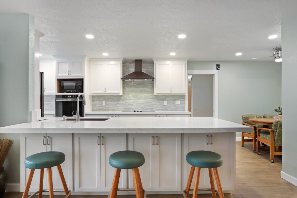 Modern galley kitchen/diner in Sacramento with a submerged sink, white cabinets, engineered stone countertops, grey splashback, glass tiled splashback, stainless steel appliances, porcelain flooring, no island, brown floors and white worktops.